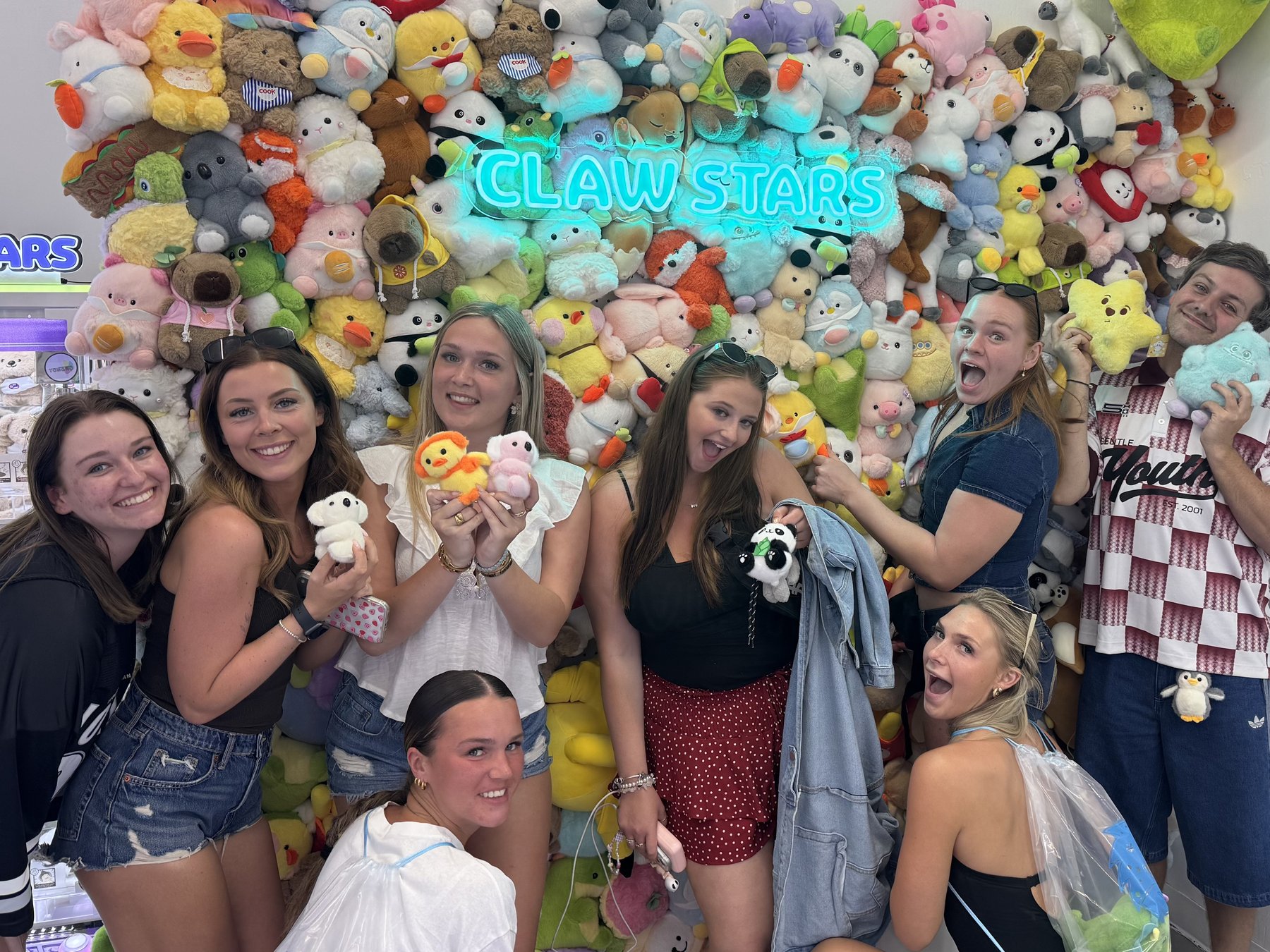 Group of friends celebrating with the plushies they just won at the Claw Stars neon wall